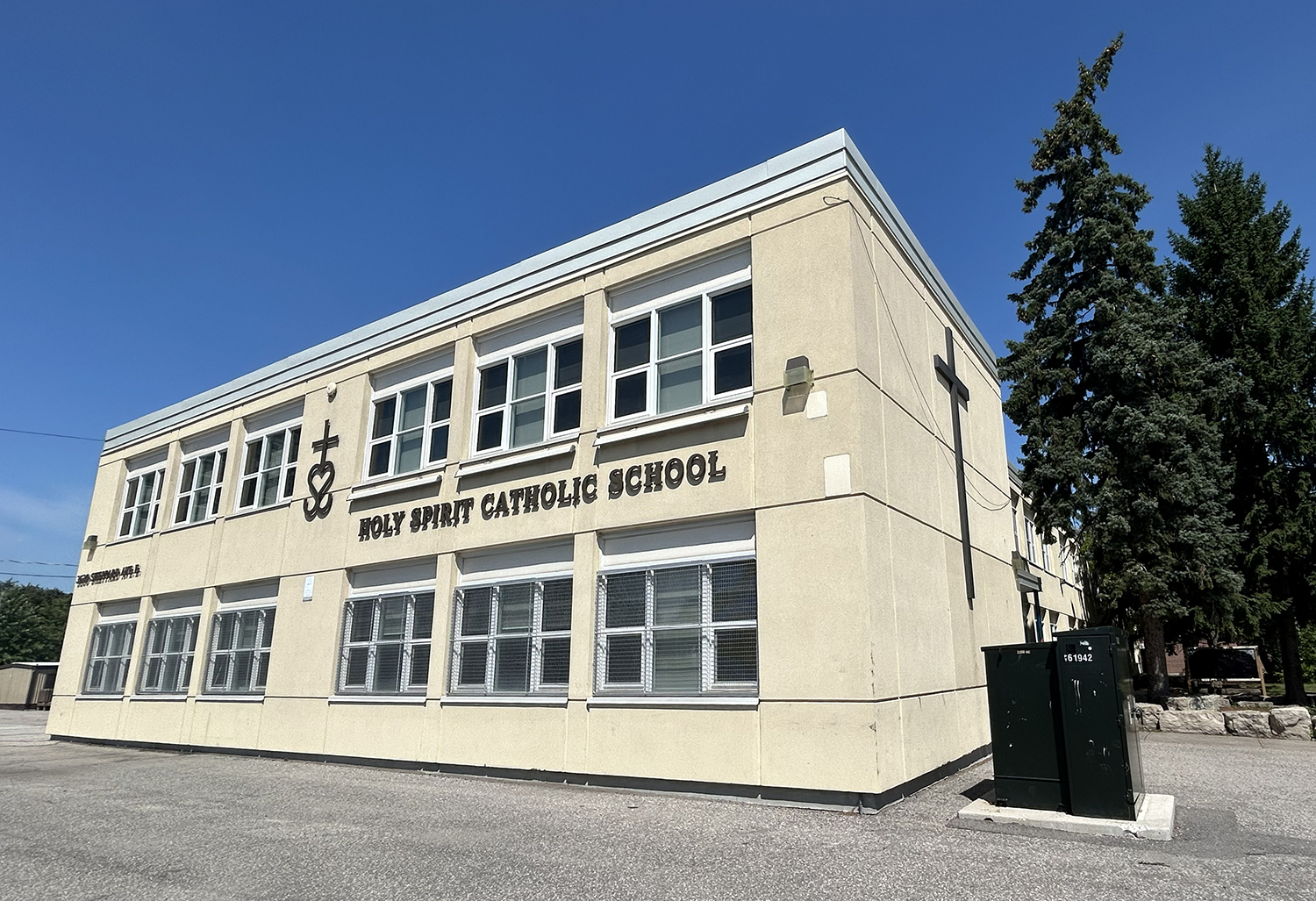 Photo of the Holy Spirit Catholic School building, a beige building looking out onto a busy road, with some trees around it and the school grounds