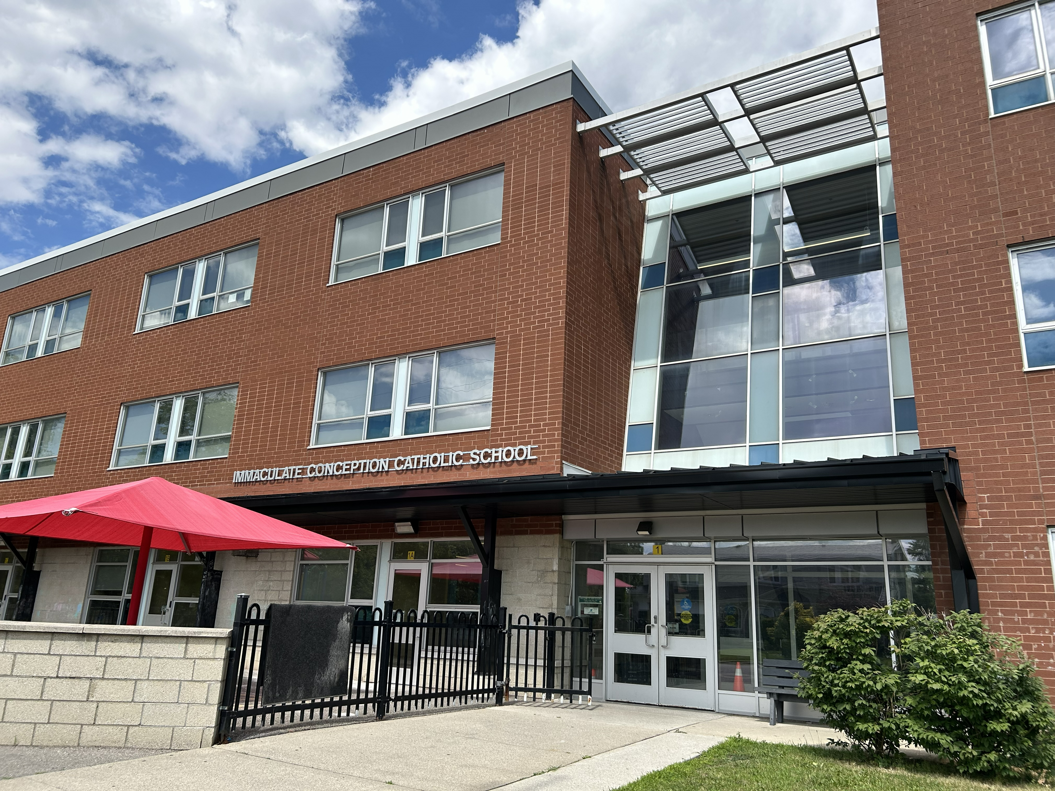 Photo of the Immaculate Conception Catholic School building, showing a red brick building with the school playground in front of it, against a blue sky