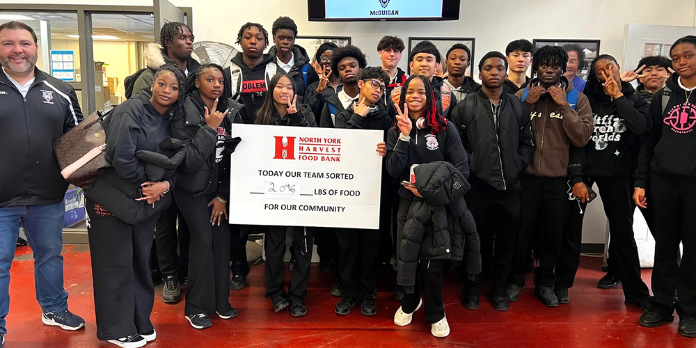 A group of students posing with a Harvest Food bank banner