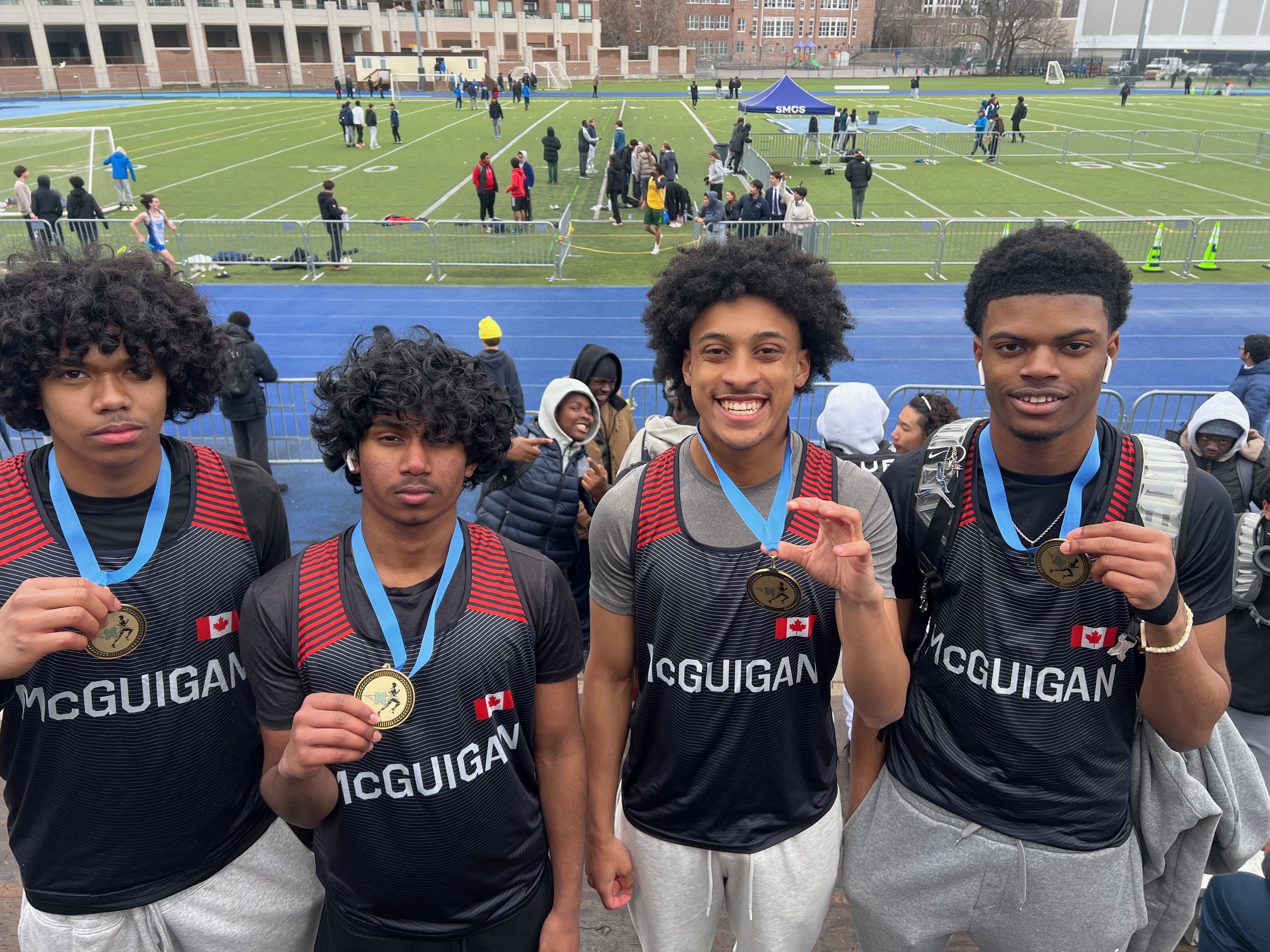4 students holding medals, on a track field