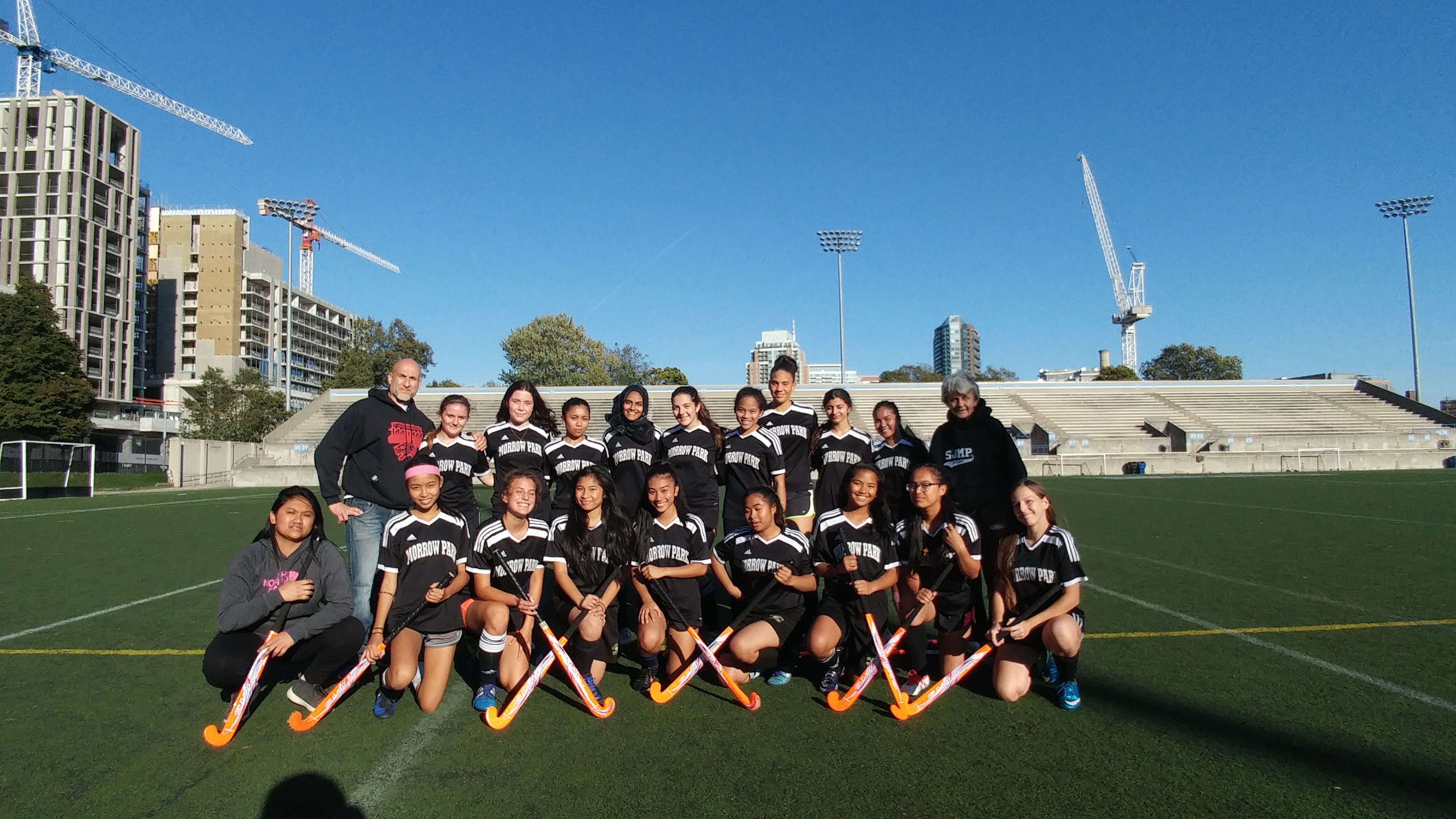 Field hockey team posing together with their uniforms and equipment on the field