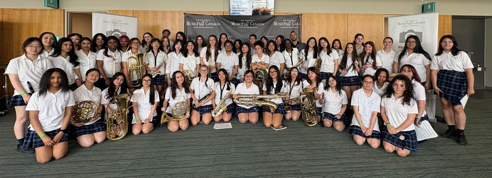 Members of a school concert band and their conductor pose with woodwind, brass, and percussion instruments at the MusicFest Canada National Finals. .