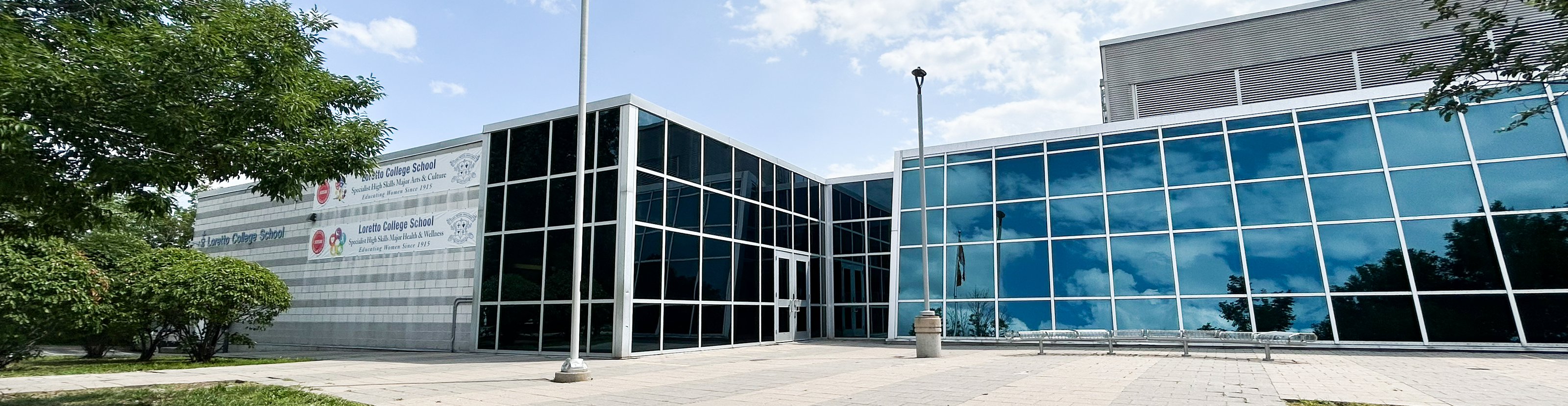 Photo of Loretto College School, showing a sprawling white and glass building surrounded by trees, in a residential area, with banners on the front advertising the SHSM programs offered at the school