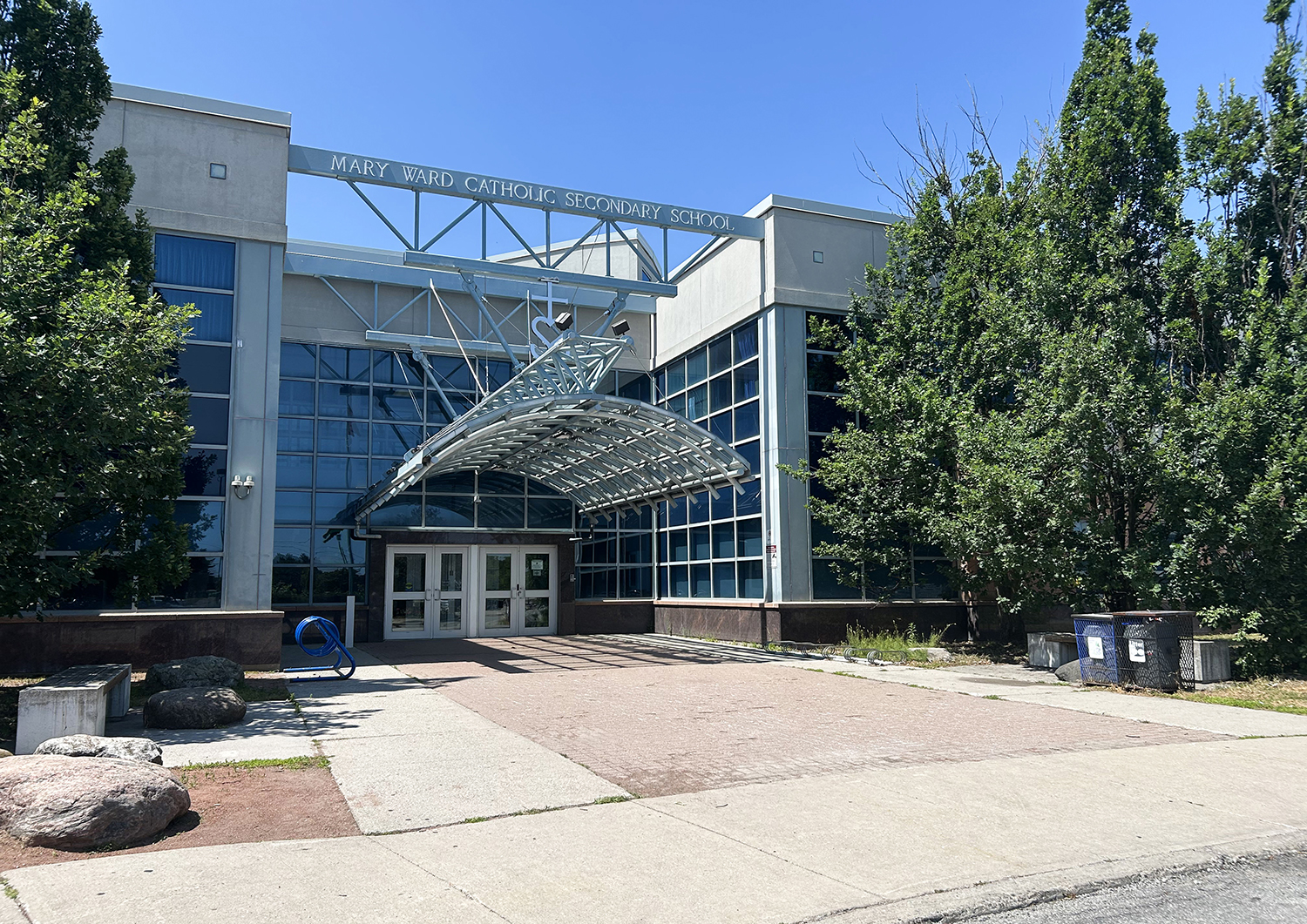 Photo of Mary Ward Catholic Secondary School, showing a mostly white and glass building nestled between trees in a scenic park area
