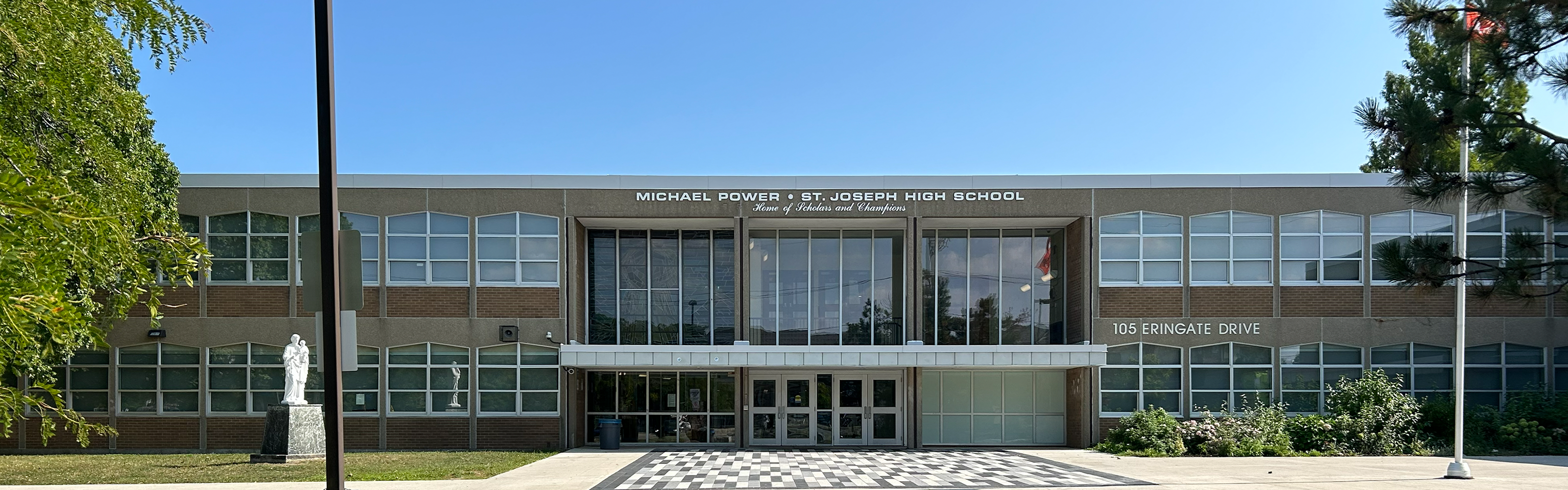 Photo of the Michael Power St. Joseph High School building, show the beige stone building front the front, with the school name in white above the front doors, and bordered by trees