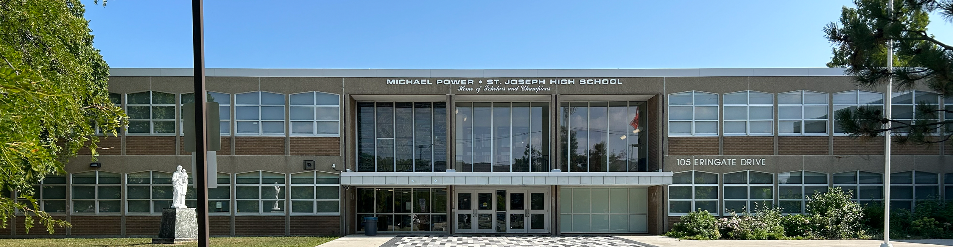 Photo of the Michael Power St. Joseph High School building, show the beige stone building front the front, with the school name in white above the front doors, and bordered by trees