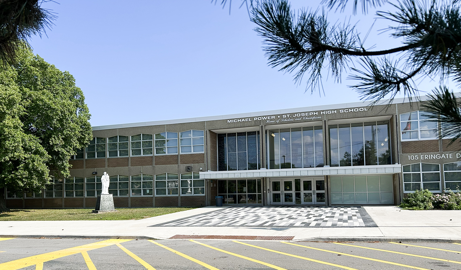 Photo of the Michael Power St. Joseph High School building, show the beige stone building front the front, with the school name in white above the front doors, and bordered by trees