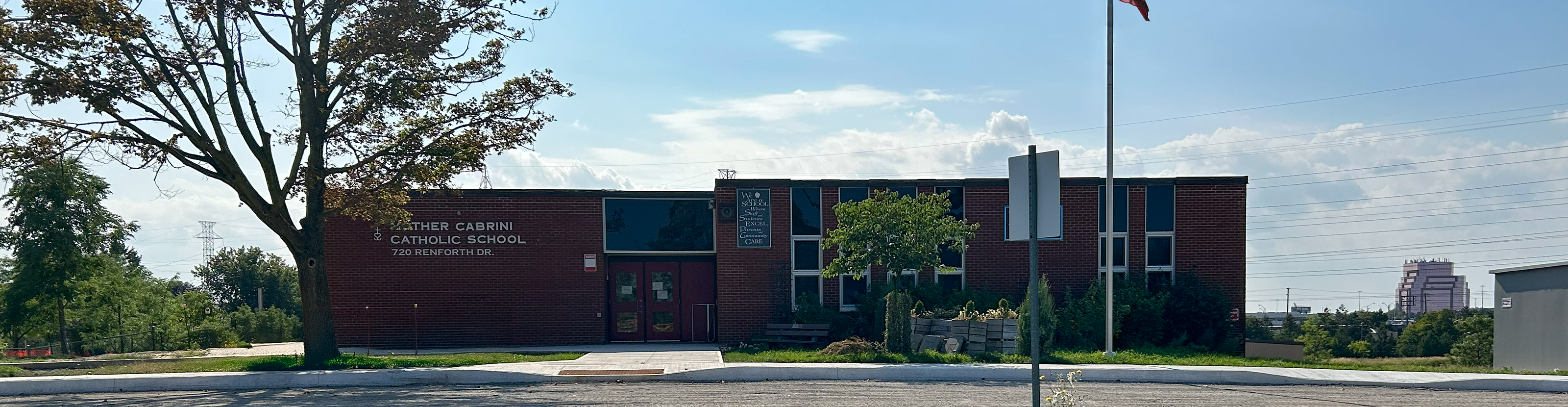 The front of the Mother Cabrini Catholic School building, showing the red brick building against a sunny blue sky with expansive green ground beyond