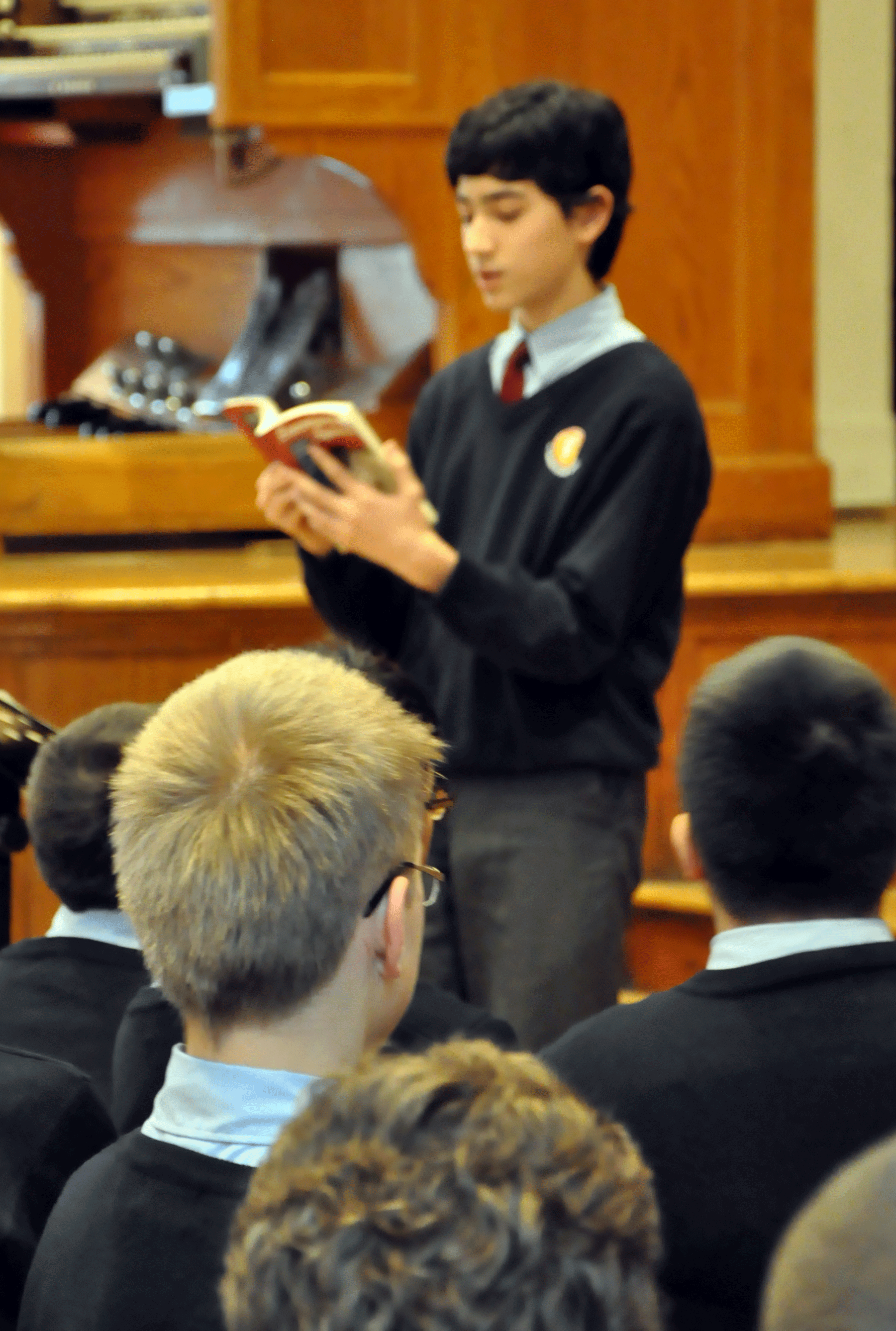 Student in uniform reading a book in front of people.