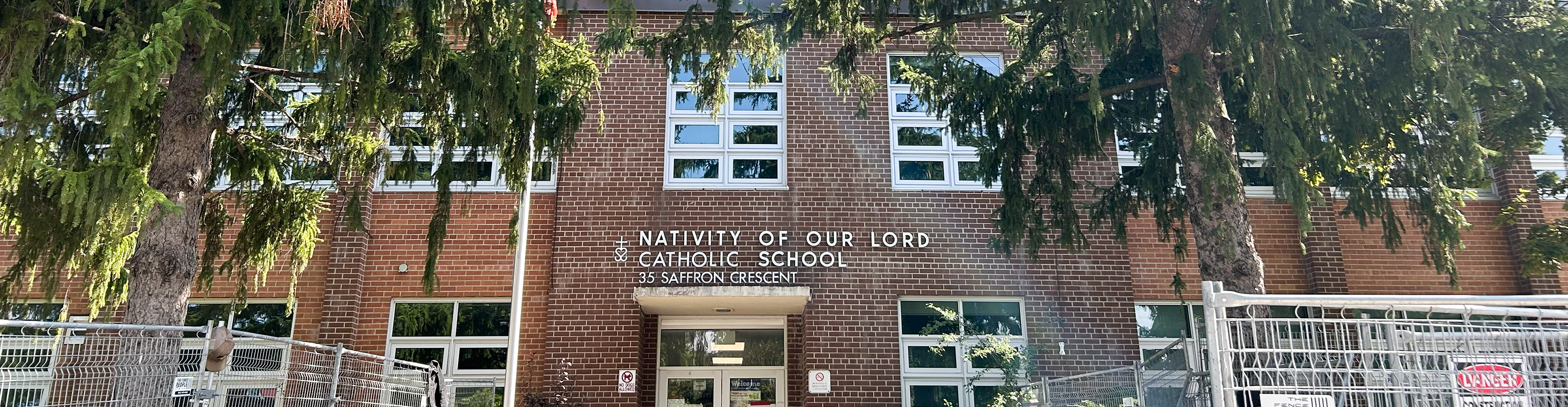 Photo of the Nativity of Our Lord Catholic School building, showing the red brick building nestled between tall trees, with the school name and address in white above the front door