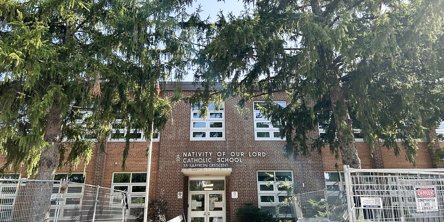 Photo of the Nativity of Our Lord Catholic School building, showing the red brick building nestled between tall trees, with the school name and address in white above the front door