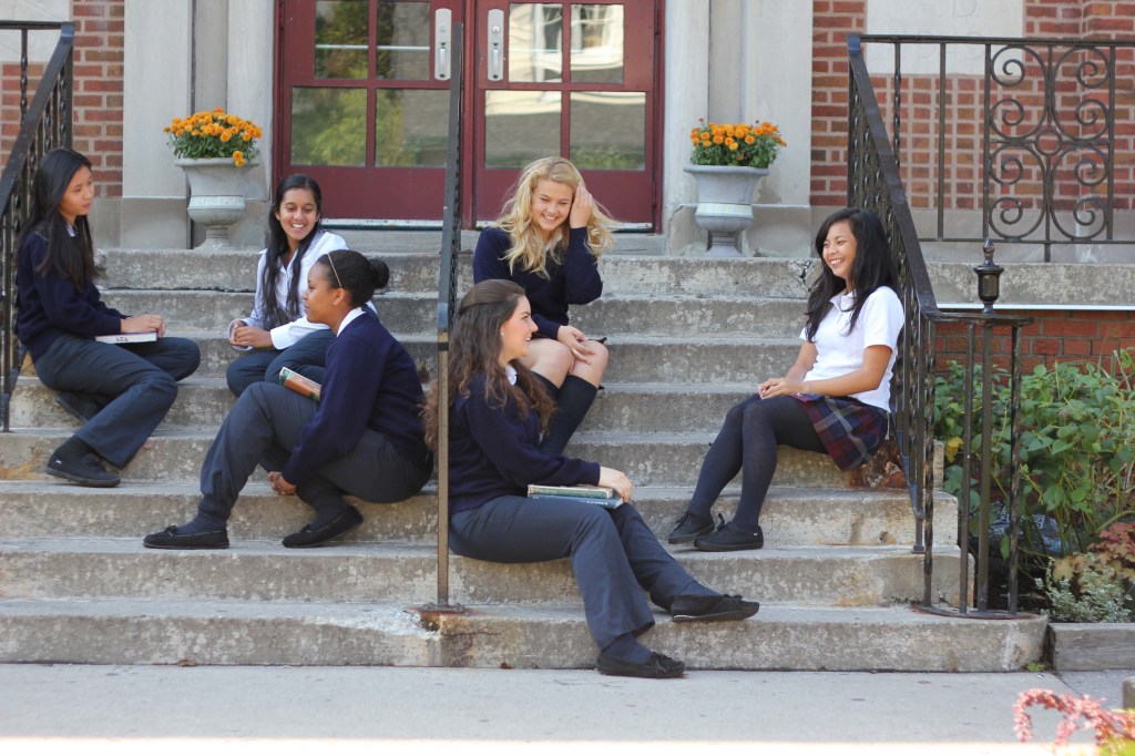 Six students in uniform sitting on stairs outside