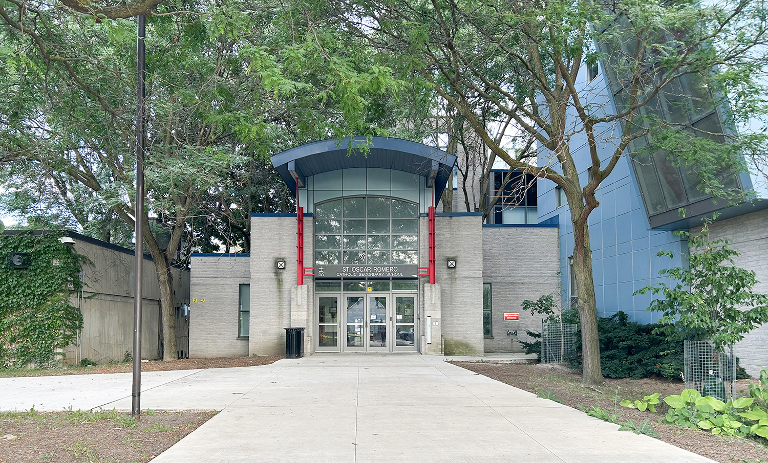 Photo of the front entrance of the St. Oscar Romero Catholic Secondary School building, showing the light grey stone building nestled between trees