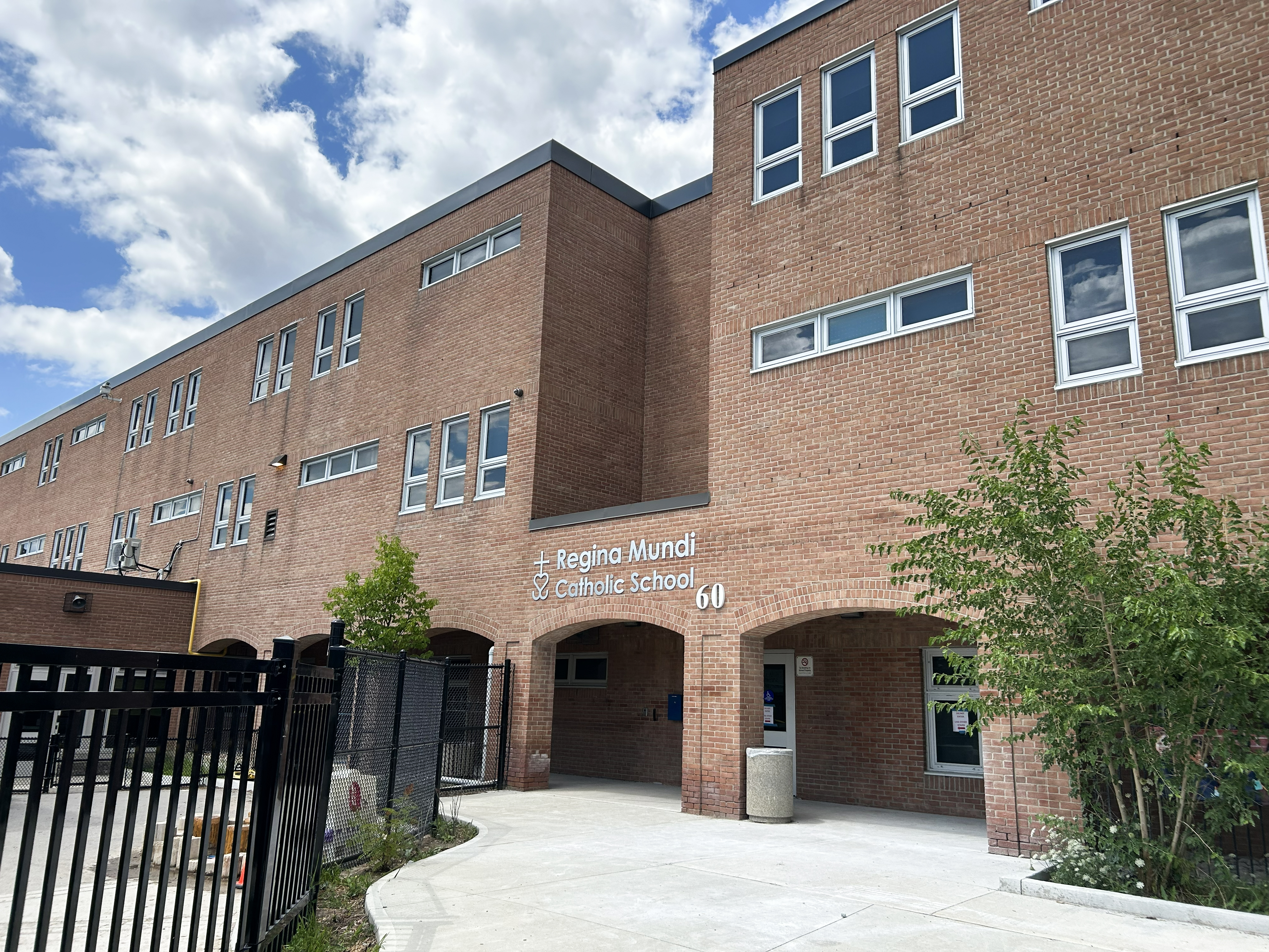 The front of the Regina Mundi Catholic School building, showing a sunlit light brown brick building bordered with trees