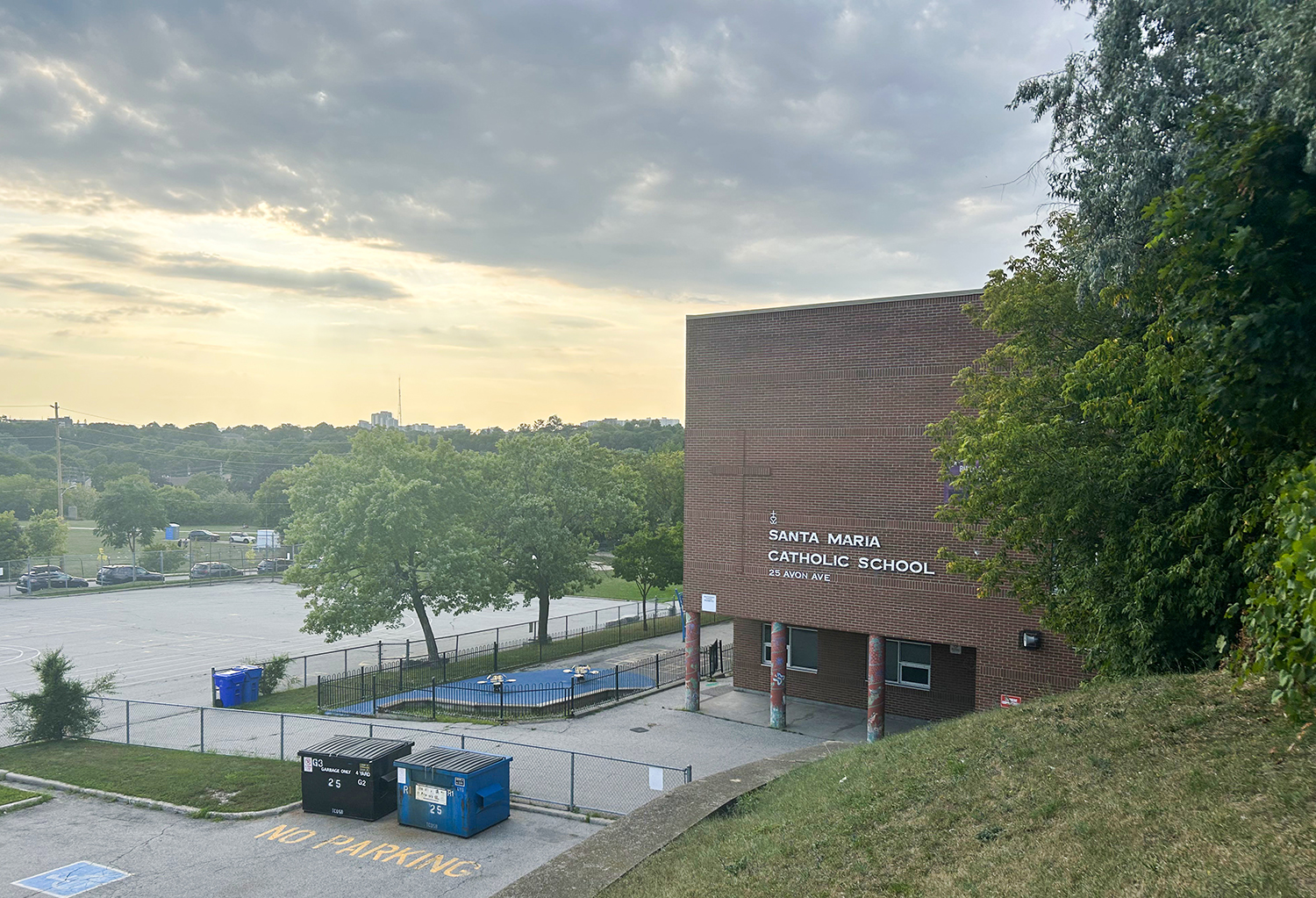 Photo of the Santa Maria Catholic School building, a red brick building with the school name in white on the front, against a vibrant blue and yellow sunset background
