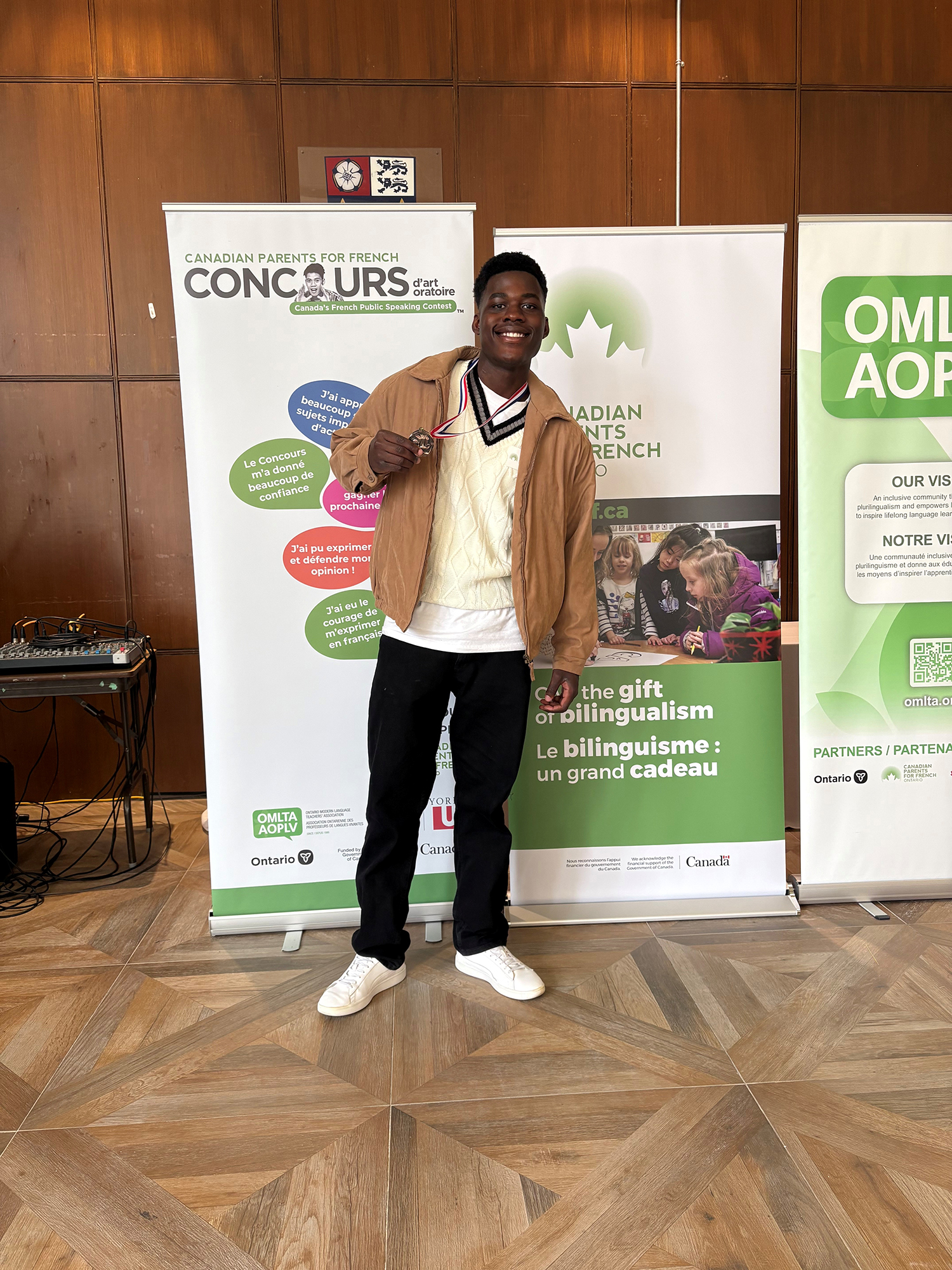 Photo of a student wearing his medal from the Concours contest, standing in front of the contest banners