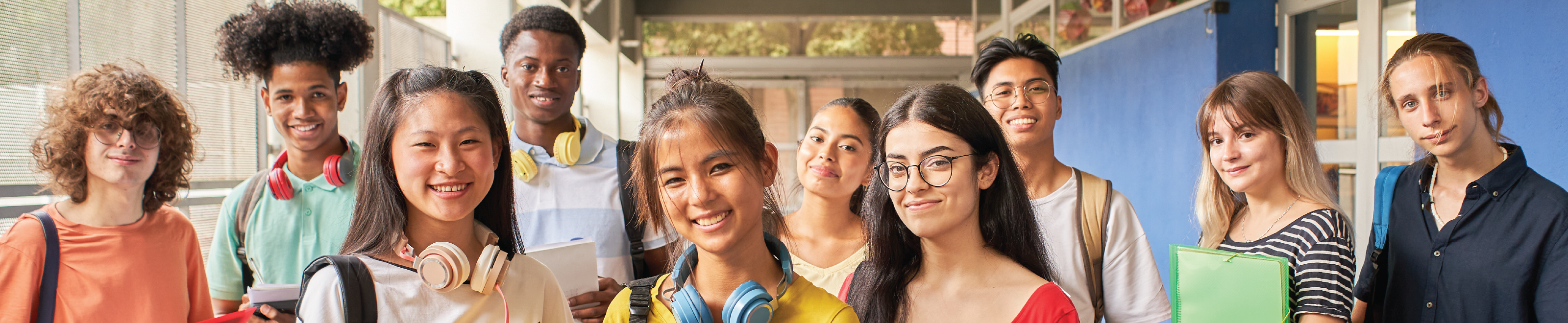 Ten students posing with classroom materials and backpacks in a school hallway.