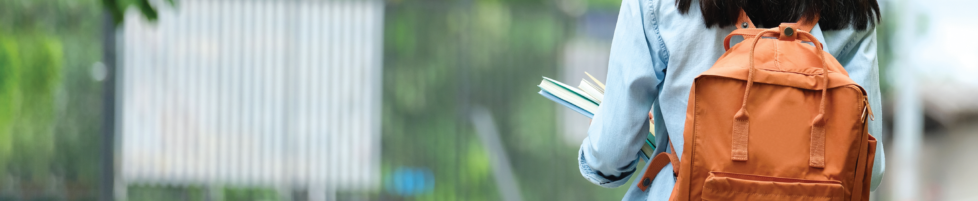 A photo shot from behind of a student wearing a backpack and holding books.