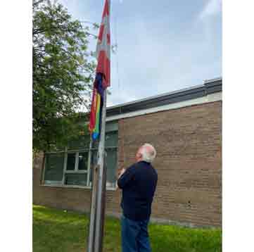 A man raising the Pride flag and the Canadian flag