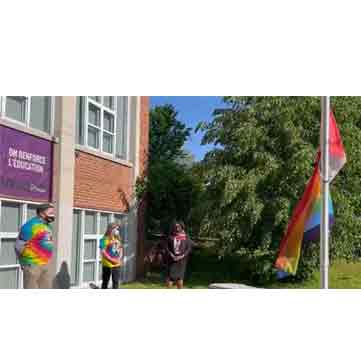 3 people looking at a flagpole with the Pride flag