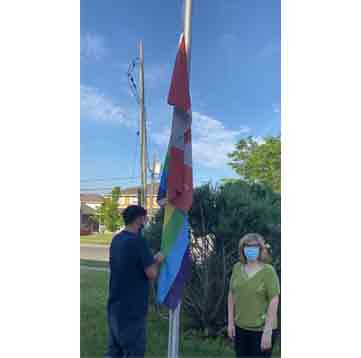 A student raising the Pride flag while a woman stands nearby