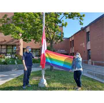 A woman holding out the Pride flag while it's on the flagpole