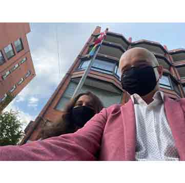 A selfie of a man and a woman with face masks on and the flagpole in the background