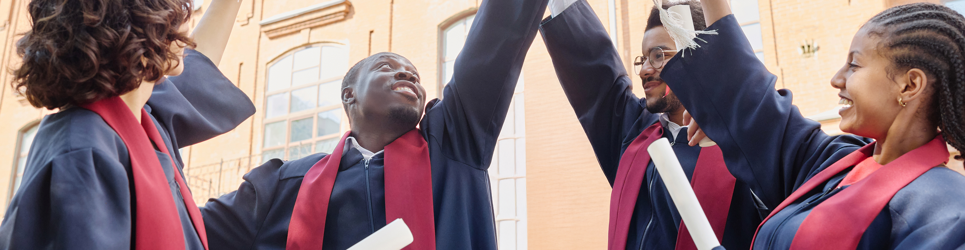 Photo of four students in graduating robes throwing up their mortarboards into the air in celebration