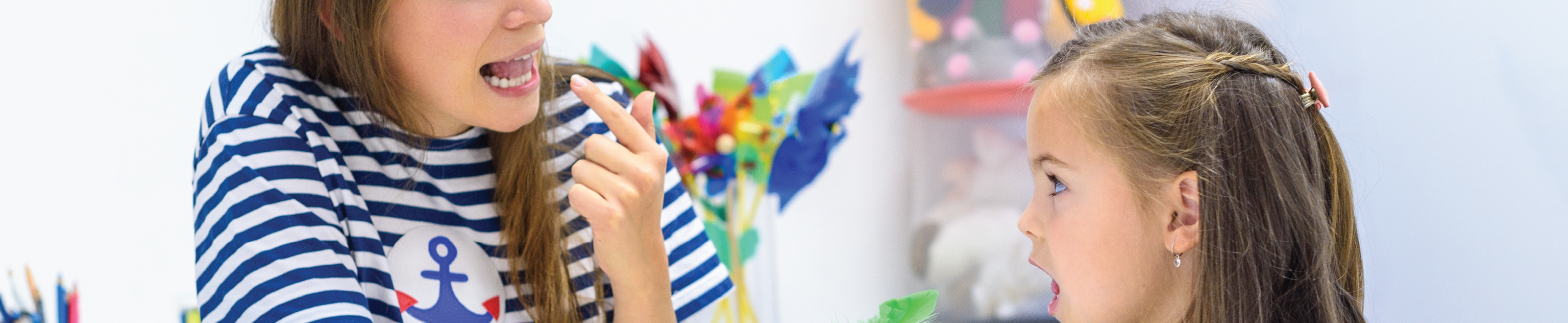 A speech therapist pointing to her tongue and helping a student.