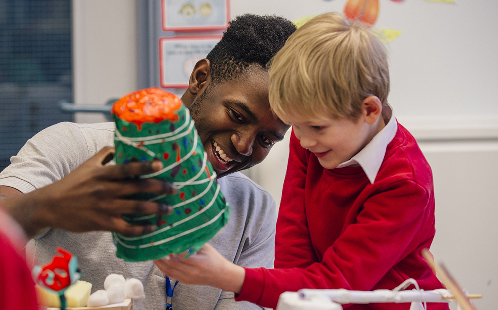 student in red sweater crafting paper christmas tree with teacher