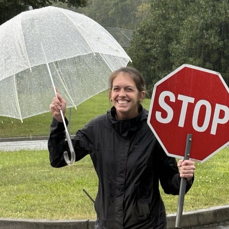 A woman poses with an umbrella and a stop sign in a wet parking lot.