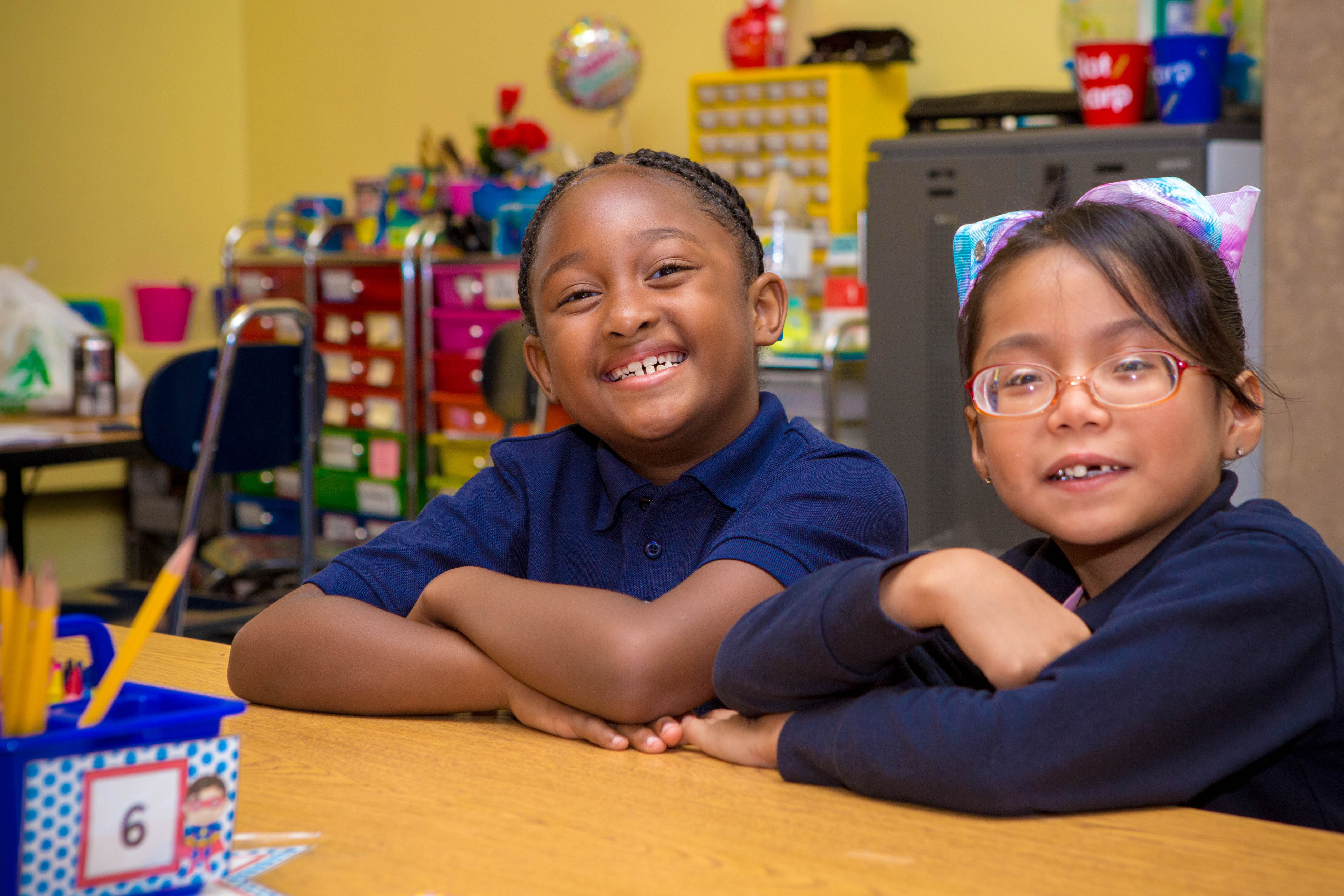 Two Scholars sitting at table in classroom smiling