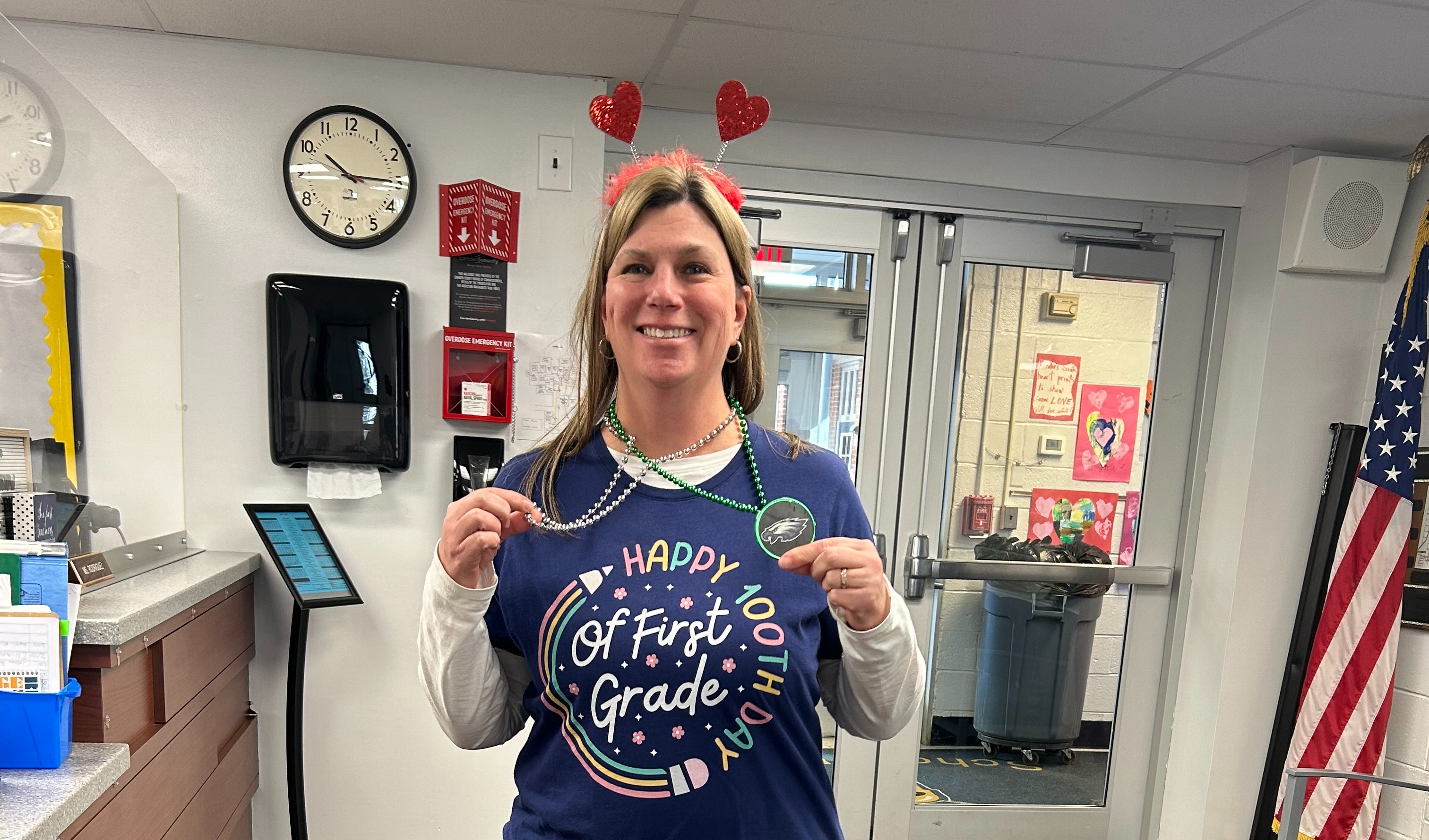Teacher holding eagles pendent 100th day shirt and valentines antennae