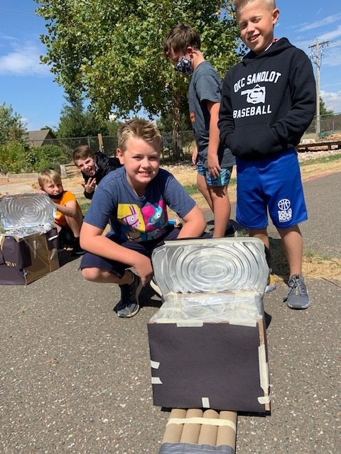 young students with homemade inventions outside