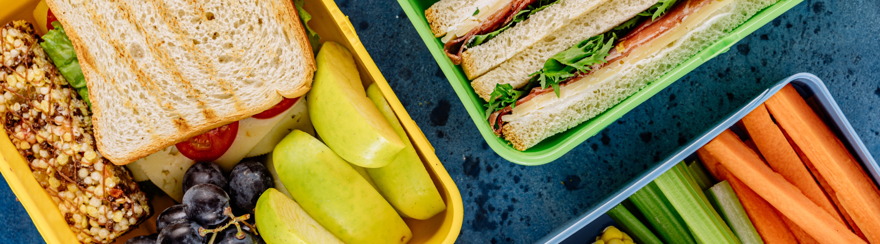 Two lunch boxes with fruit and a sandwich inside