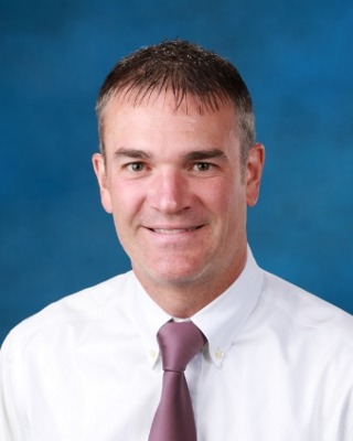 headshot of man wearing white shirt and purple tie