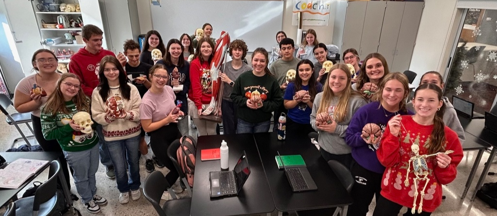 anatomy and physiology students in a classroom holding various body part models such as brains, hearts, skeletons, etc.