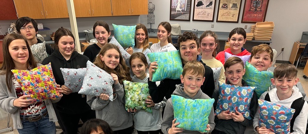 six grade students in family and consumer sciences hold up the pillows they sewed and stuffed themselves