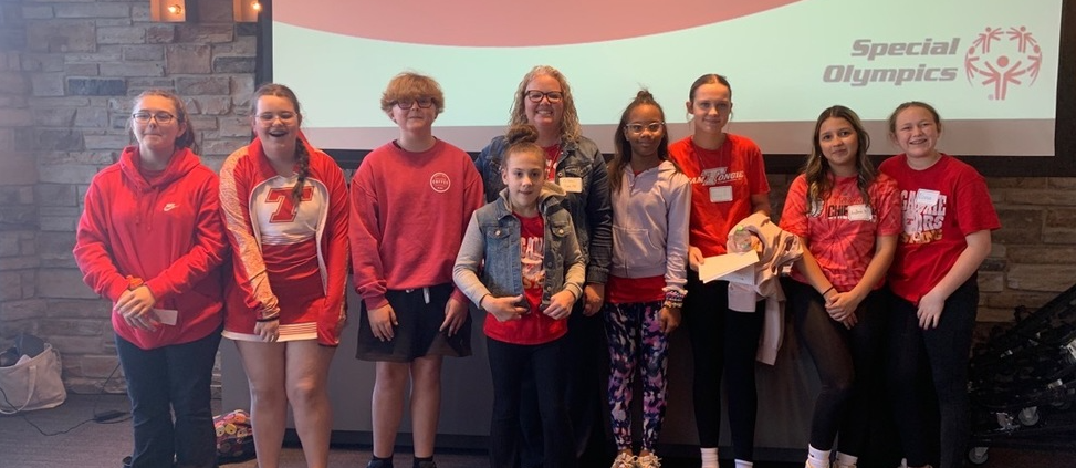 Warrior Friends students wearing red shirts, standing in front of a projection screen that says Welcome to the Metro Youth Summit