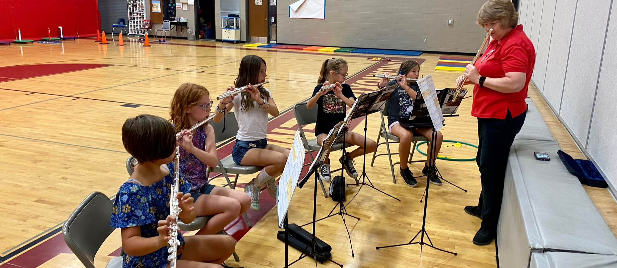 Female fifth grade students play flutes while female teacher stands in front of them