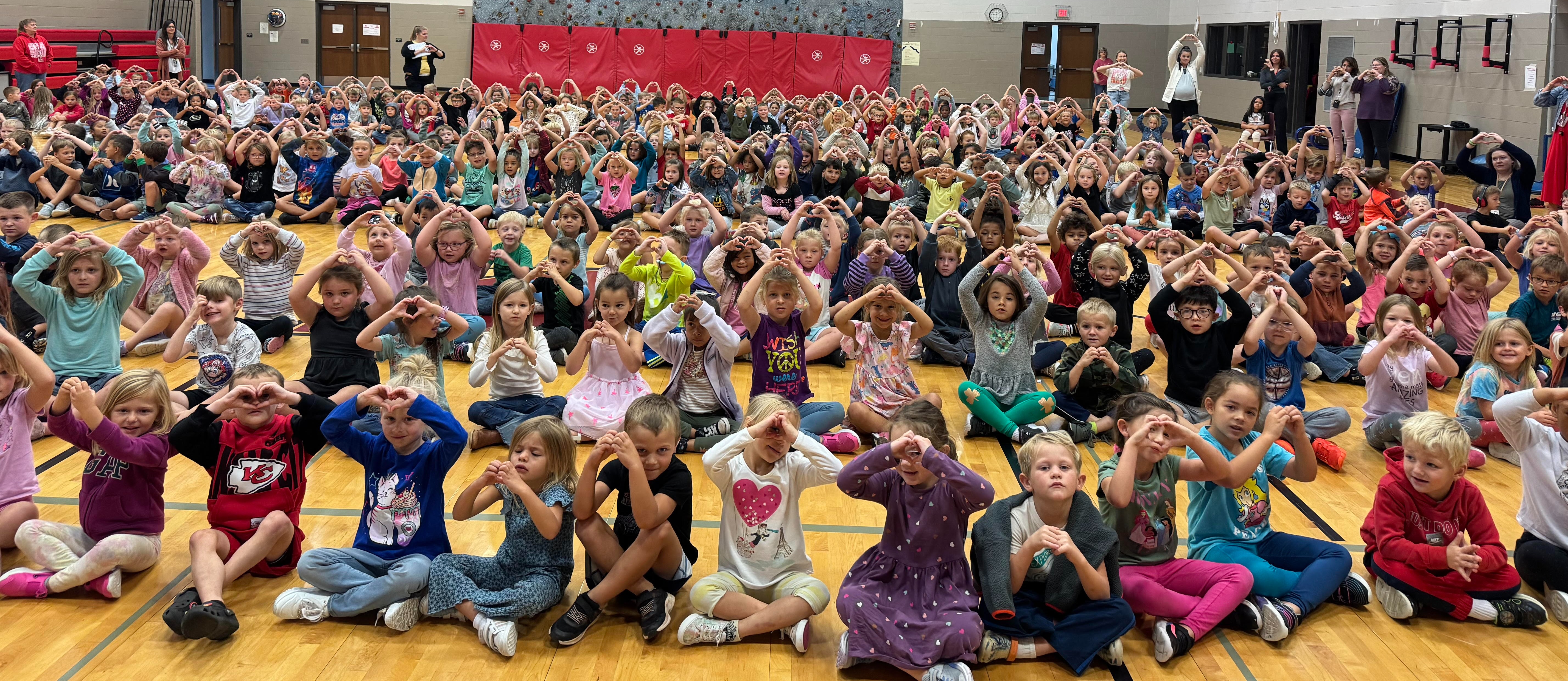 students sitting in the gym making a heart symbol with their hands