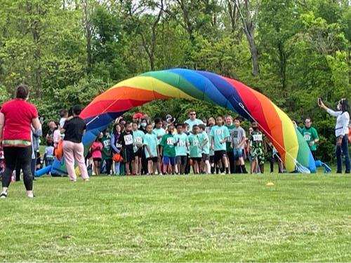 Group of students standing under rainbow colored arch 