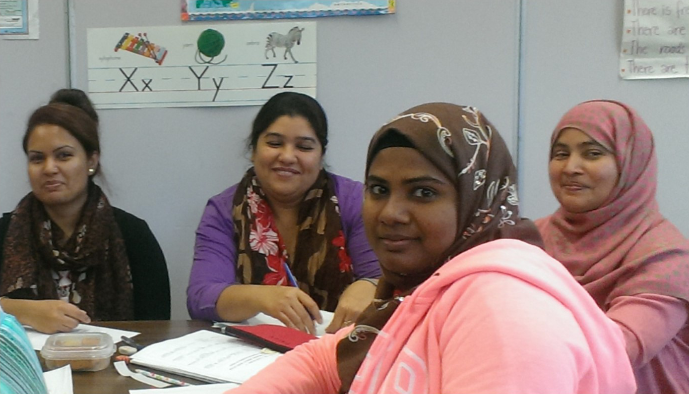 4 adult  ESL classmates at table turning and smiling for picture