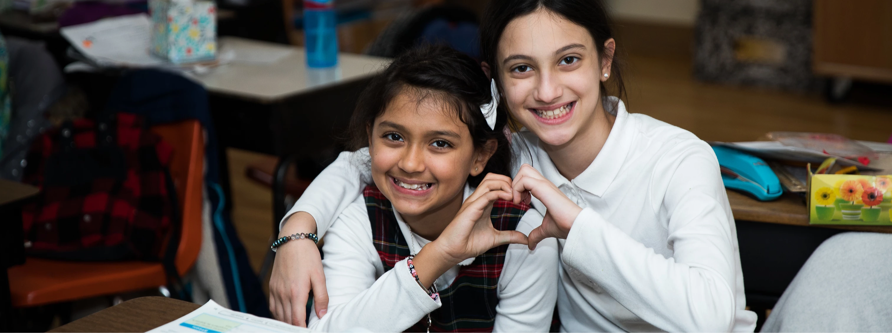 Two students making a heart shape with their hands