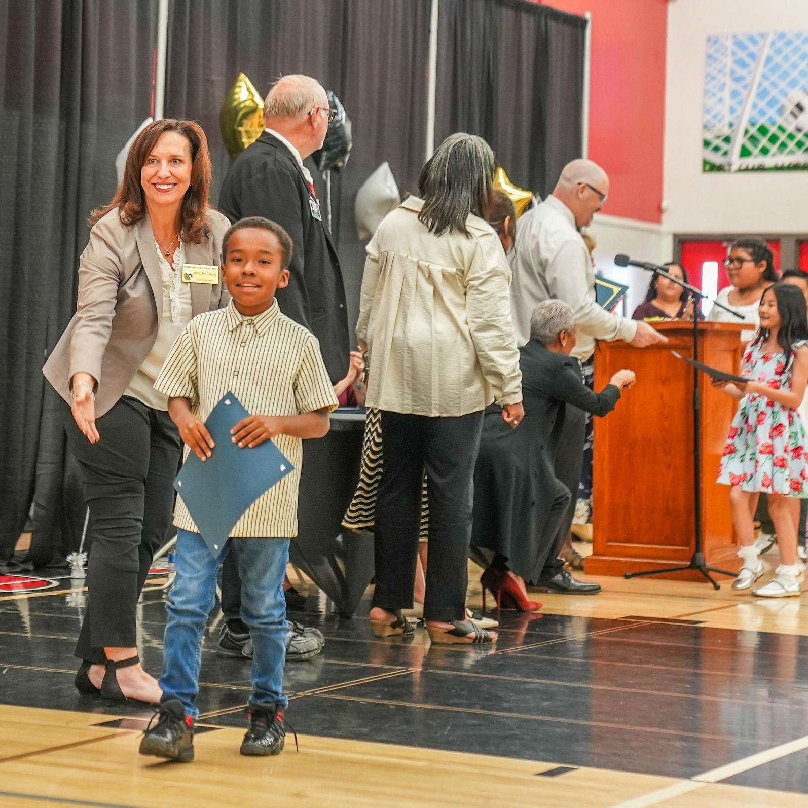 Little boy walking across the stage smiling holding his certificate