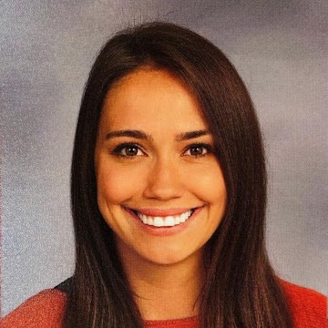 Woman with brown hair and a red top smiles with her teeth showing against a gray background.