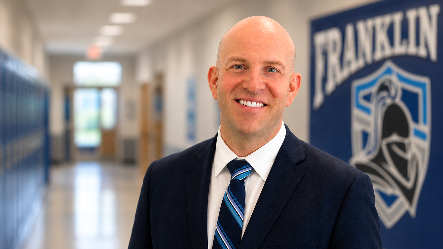 A man with a smile stands in a school corridor, facing a wall with a Franklin logo.