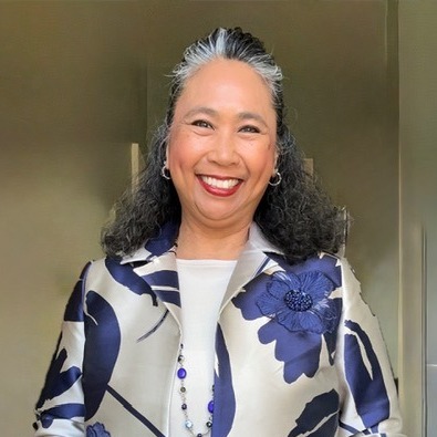 A woman with gray hair wearing a blue and white floral jacket and a white top, smiling.