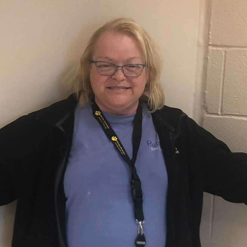 blonde woman wearing blue shirt and black jacket with arms outstretched