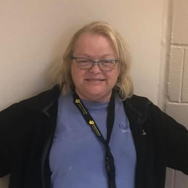 Woman with blonde, side-parted hair, wearing black jacket and lanyard with blue shirt